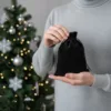 Kleines schwarzes Samtsackerl präsentiert auf der Hand vor dem Christbaum.