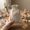Leinen Säckchen in der Hand gehalten vor kreativen Bastelmaterialien und Malzubehör