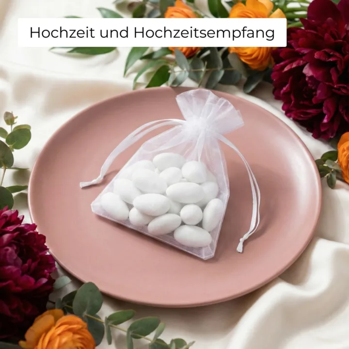 Weißes Organzasäckchen mit Hochzeitsmandeln auf einem rosa Teller.